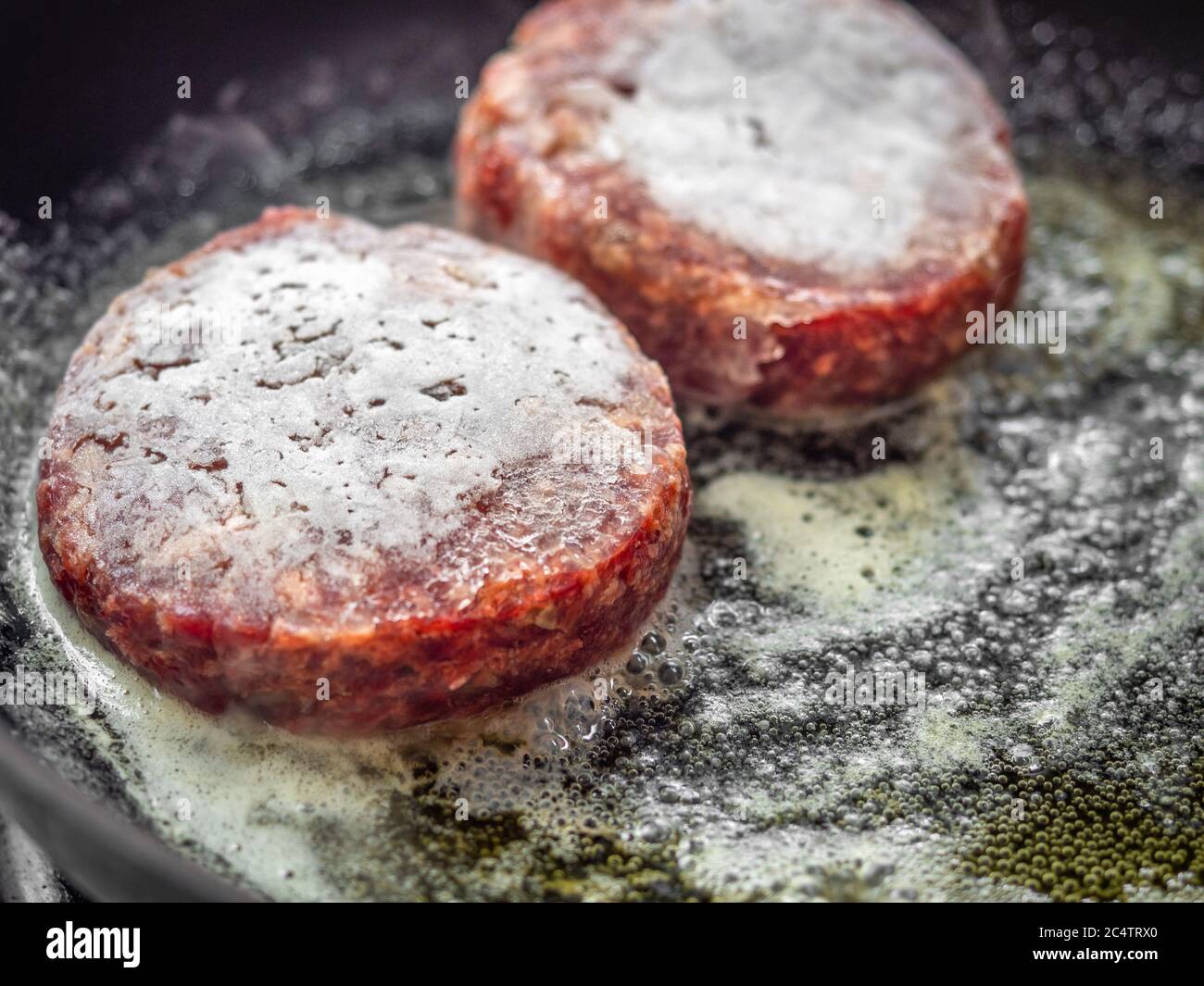 Frozen fresh beef burgers just fried in frying pan. Close-up homemade juicy minced meat patties burgers in iron frying pan. Stock Photo