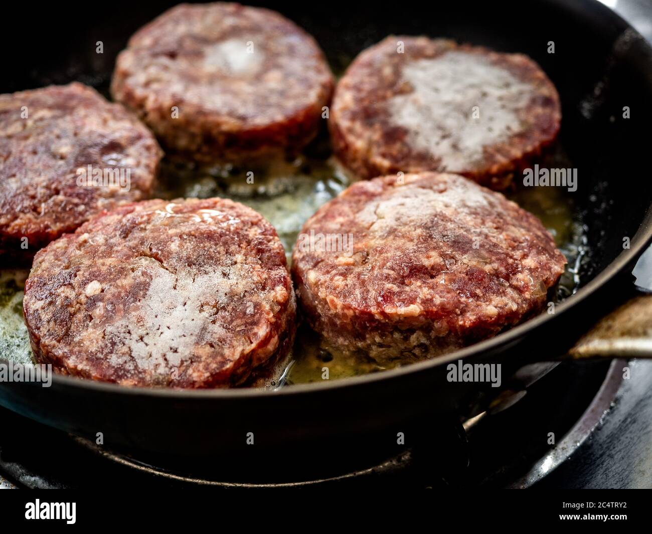 Frozen beef burgers just fried in frying pan. Close-up homemade juicy minced meat patties burgers in iron frying pan. Stock Photo