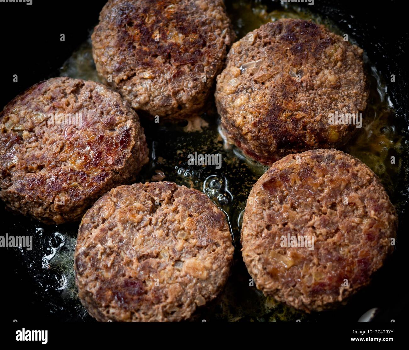 Beef burgers fried in frying pan. Close-up homemade juicy minced meat patties burgers in iron frying pan top view. Stock Photo