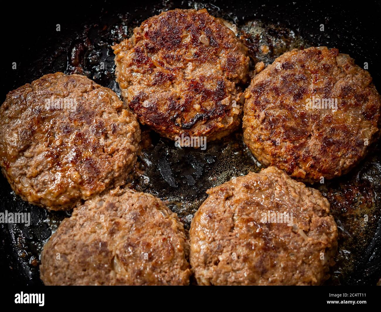 Beef burgers fried in frying pan. Close-up homemade juicy minced meat patties burgers in iron frying pan top view. Stock Photo