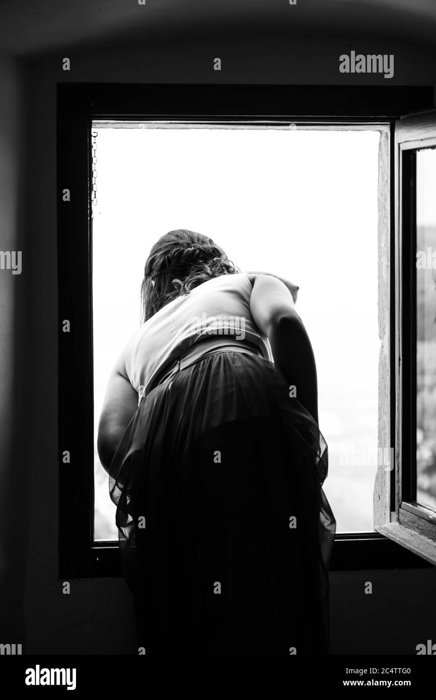 Grey scale vertical shot of a female looking out of the window Stock Photo