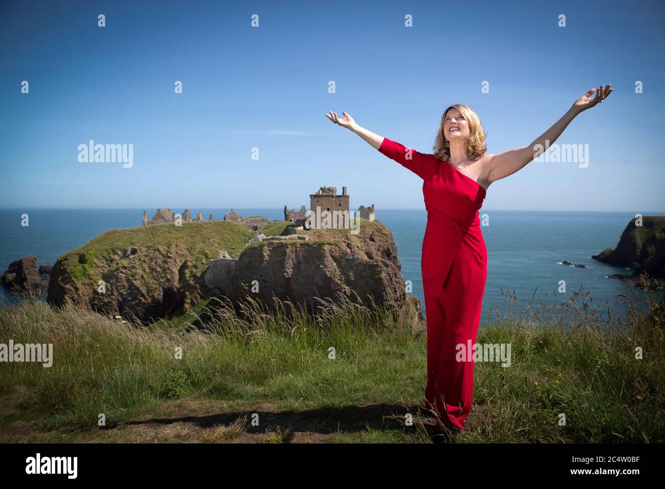 Scottish singer, song-writer and broadcaster Fiona Kennedy sings 'Stronger for the Storm', a new international song of peace, on the clifftop overlooking Dunnottar Castle on the Aberdeenshire coast, at the launch of iSing4Peace on the anniversary of the signing of the Treaty of Versailles which brought an official end to the First World War and restored peace to the world. Stock Photo
