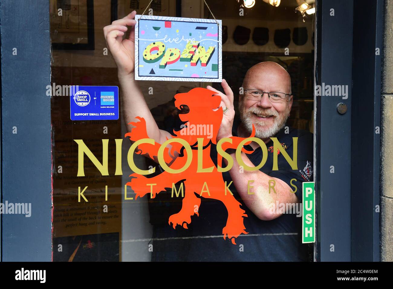 EDITORIAL USE ONLY Gordon Nicolson from Nicolson Kiltmakers in Edinburgh displays a “WE'RE OPEN” sign designed by artist Yukai Du, which has been created to celebrate the American Express Shop Small campaign and to help Scottish retailers welcome people back to our high streets. Stock Photo