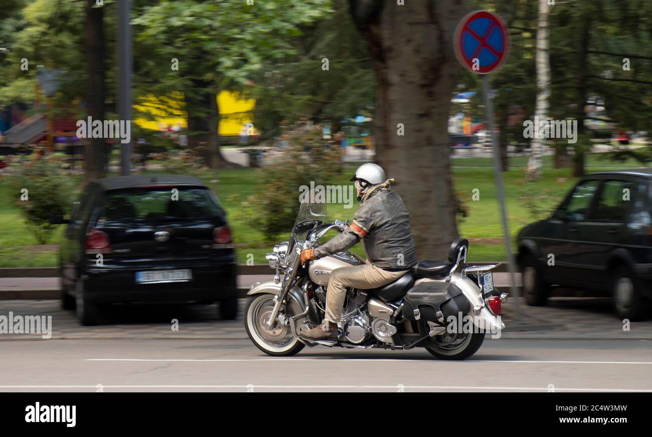Belgrade, Serbia - June 25, 2020: Mature man in leather jacket riding a double seat motorbike with side saddle bags on city street traffic, side rear Stock Photo