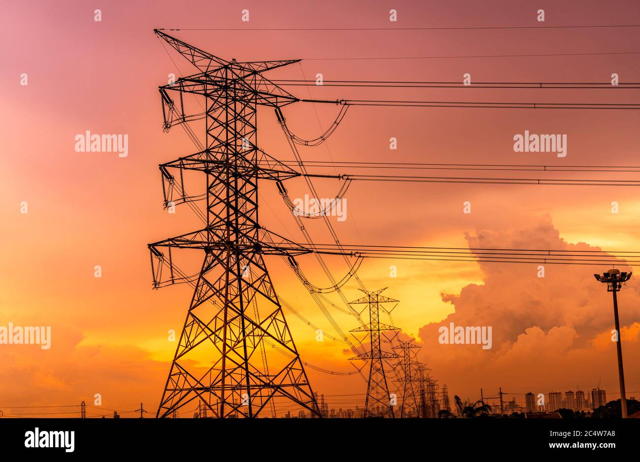 High voltage electric pylons and transmission lines with orange sunset ...