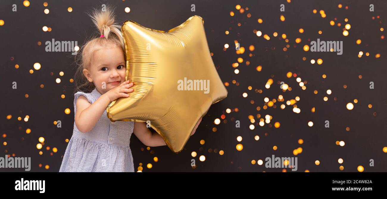 Cute blond caucasian baby with star balloon in hands at black bokeh background, Stock Photo