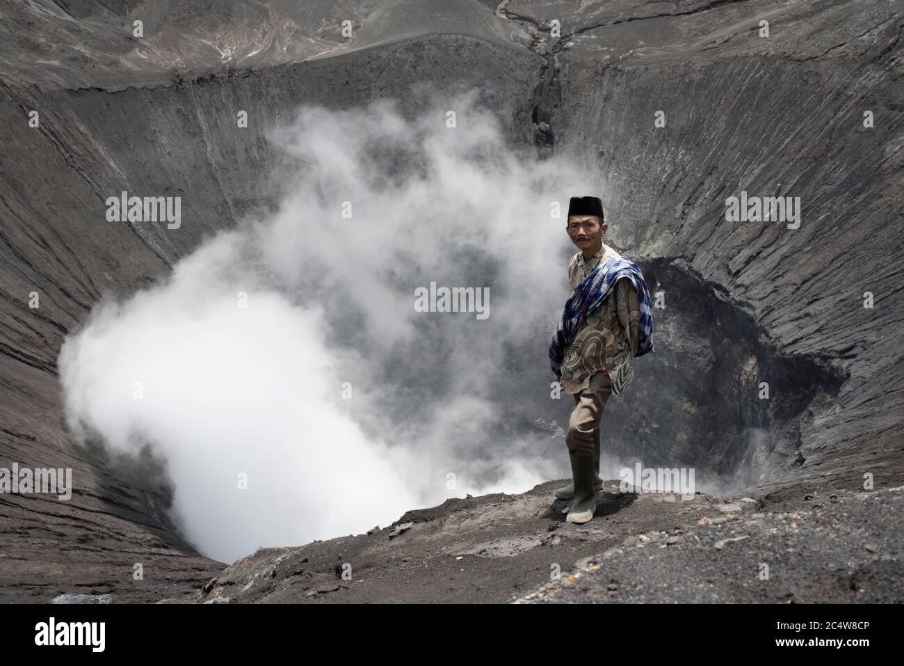 Java, Indonesia - January 17, 2014: Tenggerese Man Standing On The Edge Of An Active Volcano In Bromo Tengger Semeru National Park Stock Photo