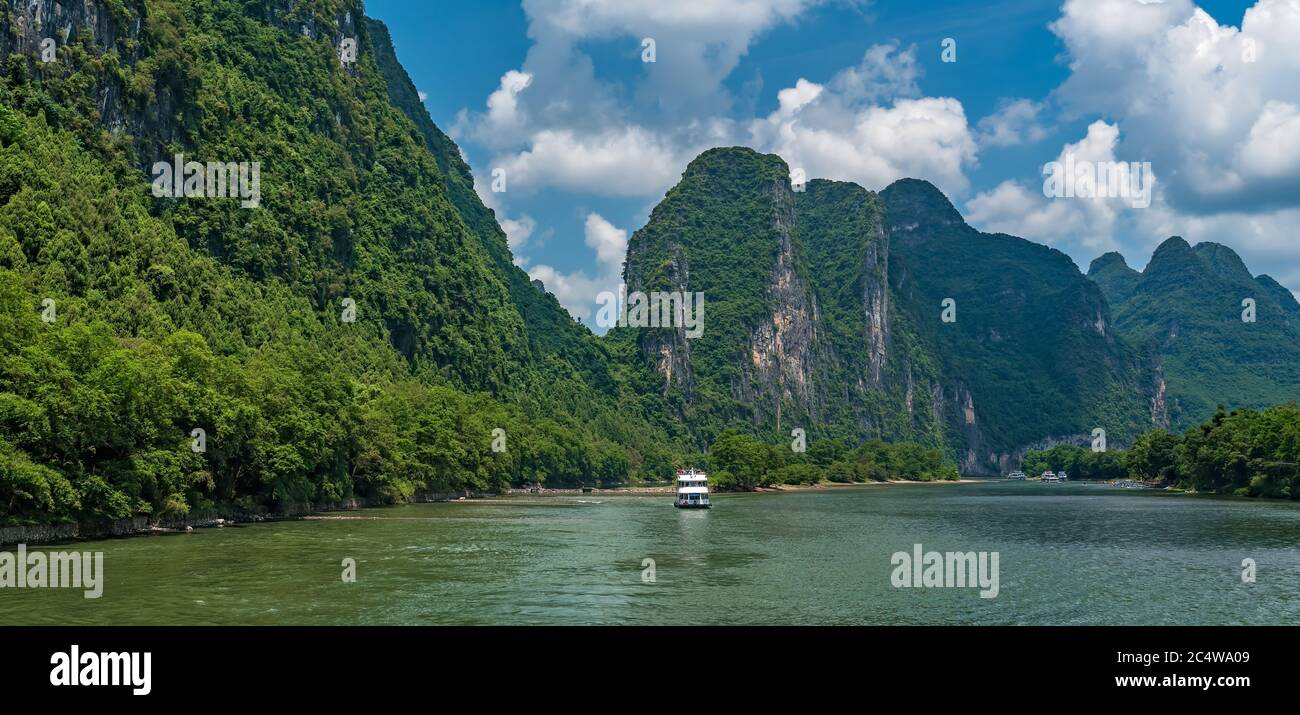 Panoramic view of sightseeing boat carrying tourists sailing among high vertical cliffs of karst mountains on the magnificent Li river flowing between Stock Photo
