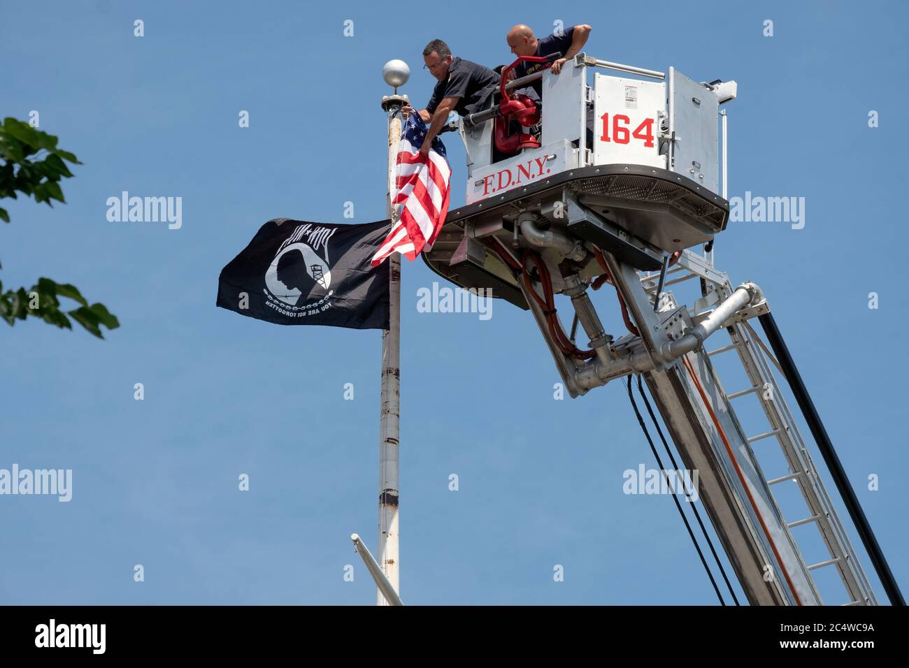 2 New York City firemen put up American and MIA POW flags high atop a pole overlooking the Bayside Marina & Cross Island Parkway. In Queens, New York. Stock Photo