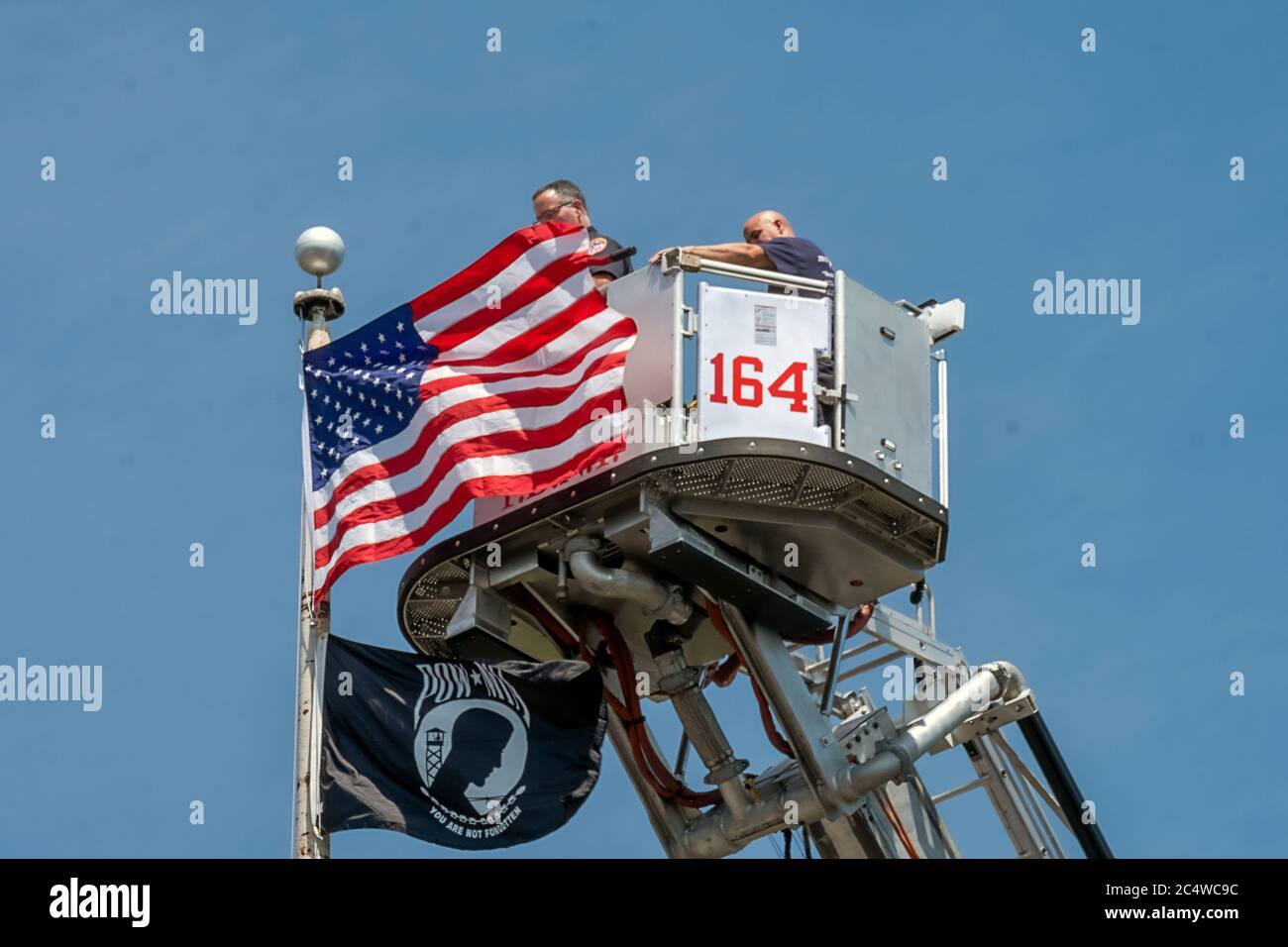 2 New York City firemen put up American and MIA POW flags high atop a pole overlooking the Bayside Marina & Cross Island Parkway. In Queens, New York. Stock Photo