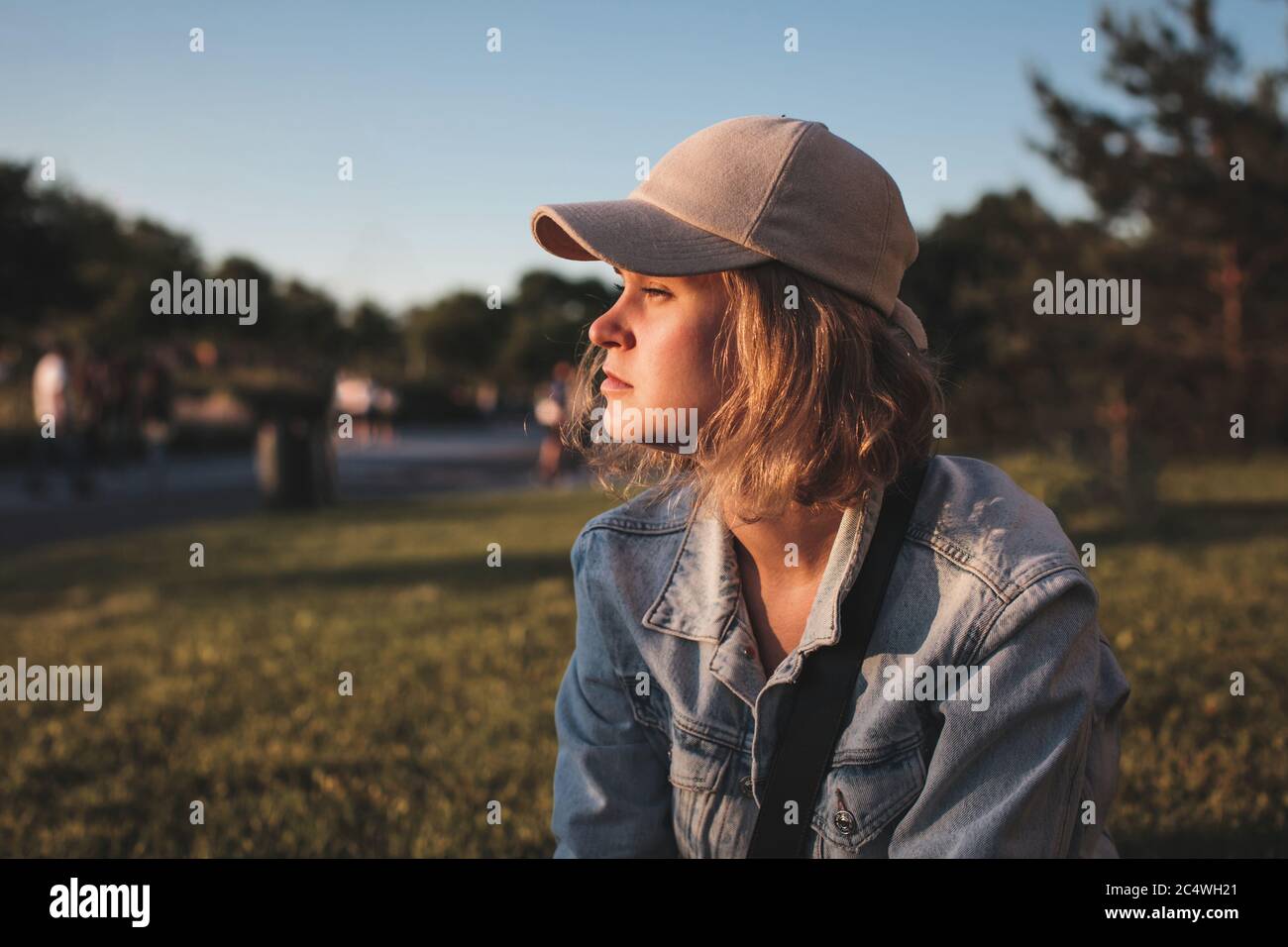 Beautiful blonde girl in a cap with short hair sits and looking away. Selective focus. Stock Photo