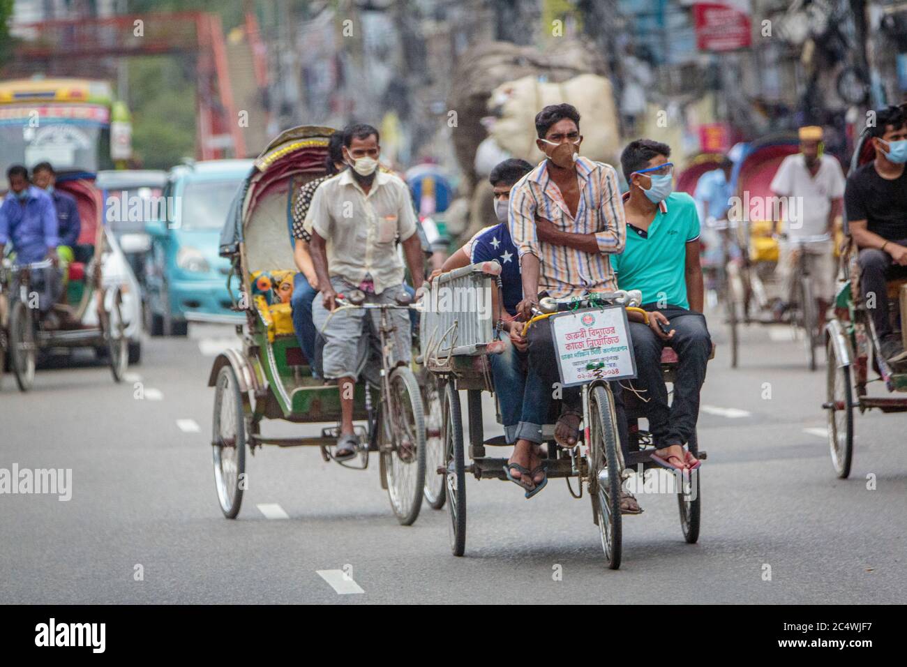 A ricksha-wala, or a rickshaw driver with his passengers on the streets of Dhaka. Residents in the Bangladesh Capital Dhaka are adjusting to the threat from the COVID 19 corona virus. Stock Photo