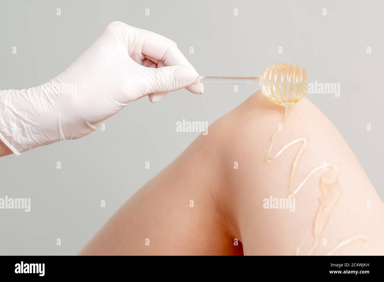 Wax on honey stick flowing down on female leg in human hand wearing protective glove on white background Stock Photo