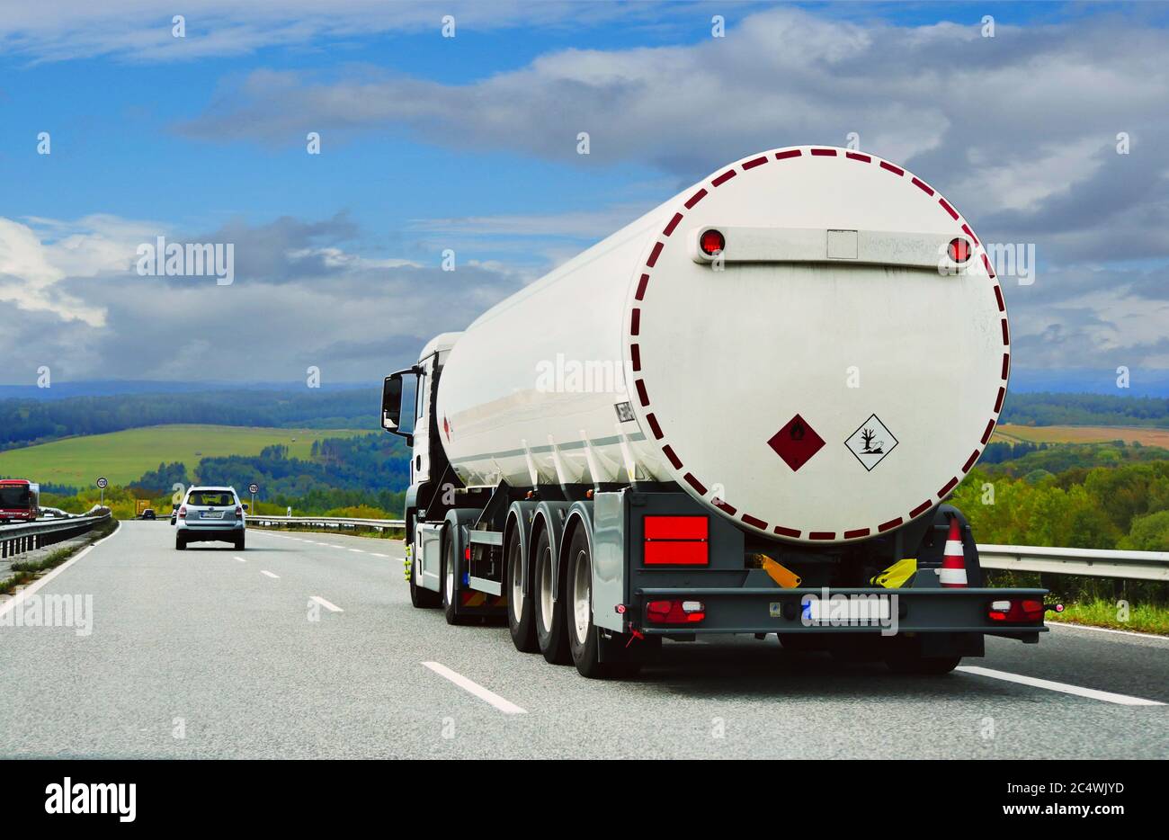 a fuel truck is driving along a beautiful road among fields, forests, and meadows. West Germany. autumn Stock Photo