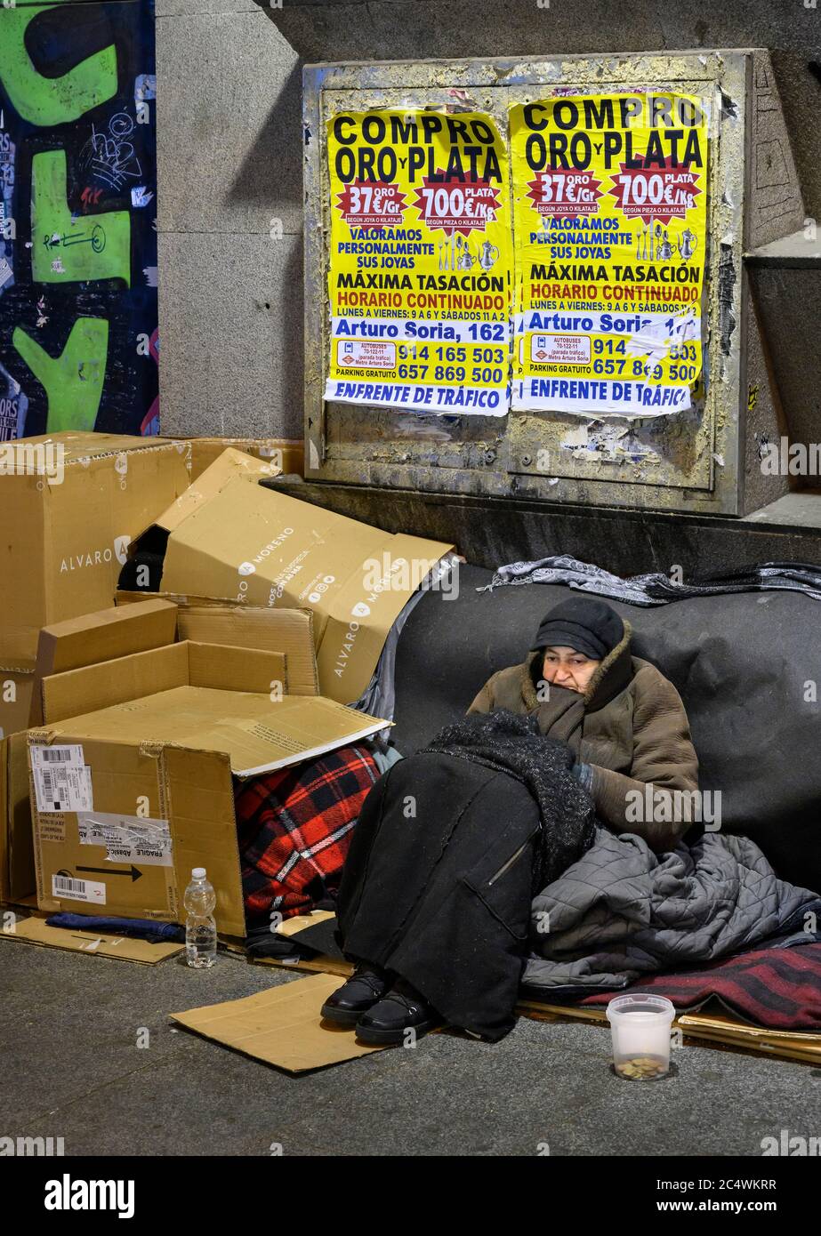 A homeless woman sleeping rough in the street, below posters advertising the purchase gold and silver, central  Madrid, Spain. Stock Photo