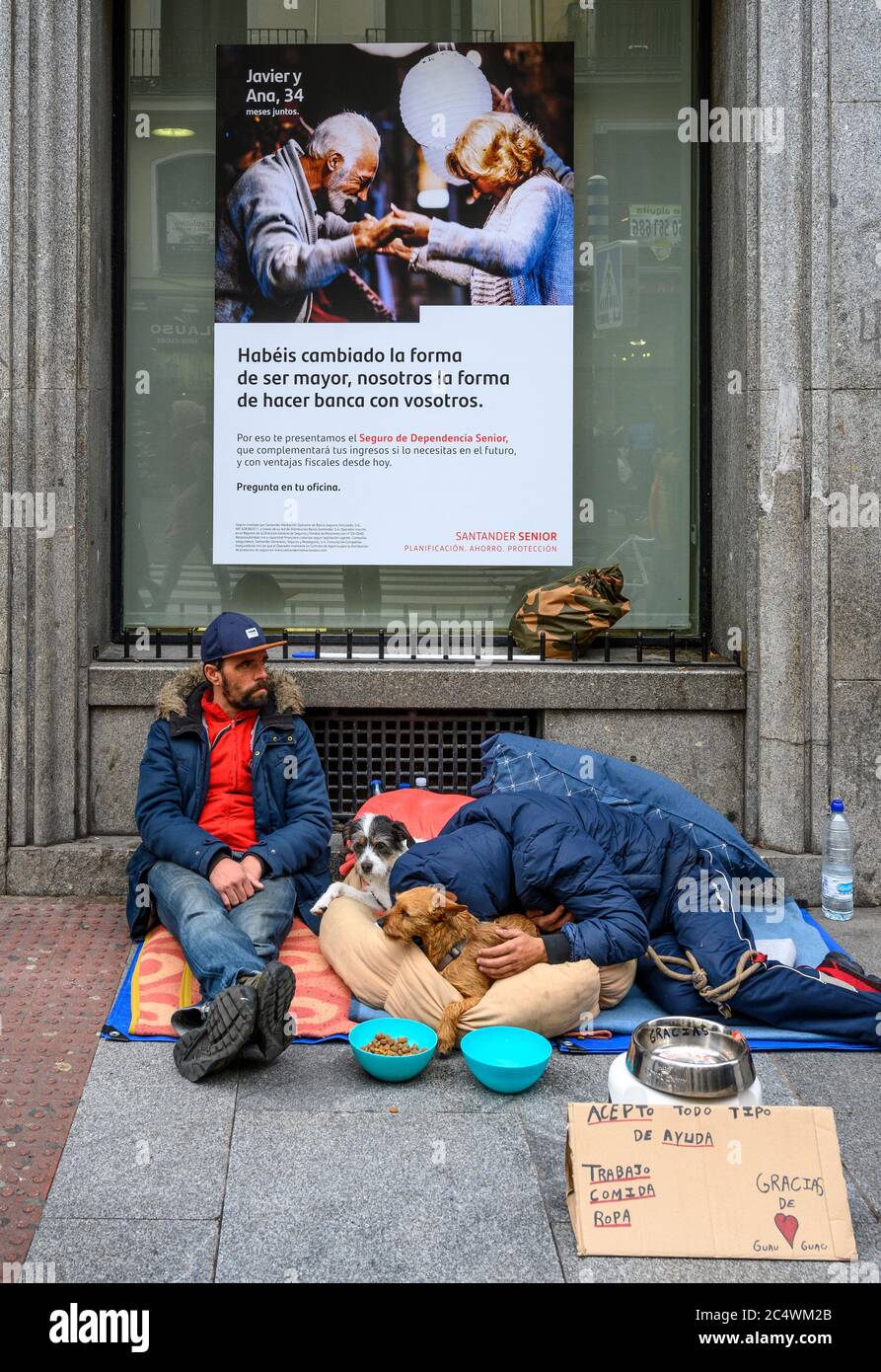 Homeless men begging with their pet dogs, below a bank advertisment in central Madrid, Spain. Stock Photo