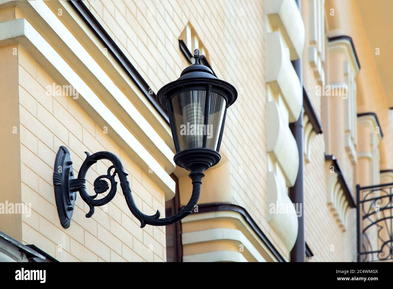 Black iron wall lamp mounted on the facade of a yellow brick building. Stock Photo