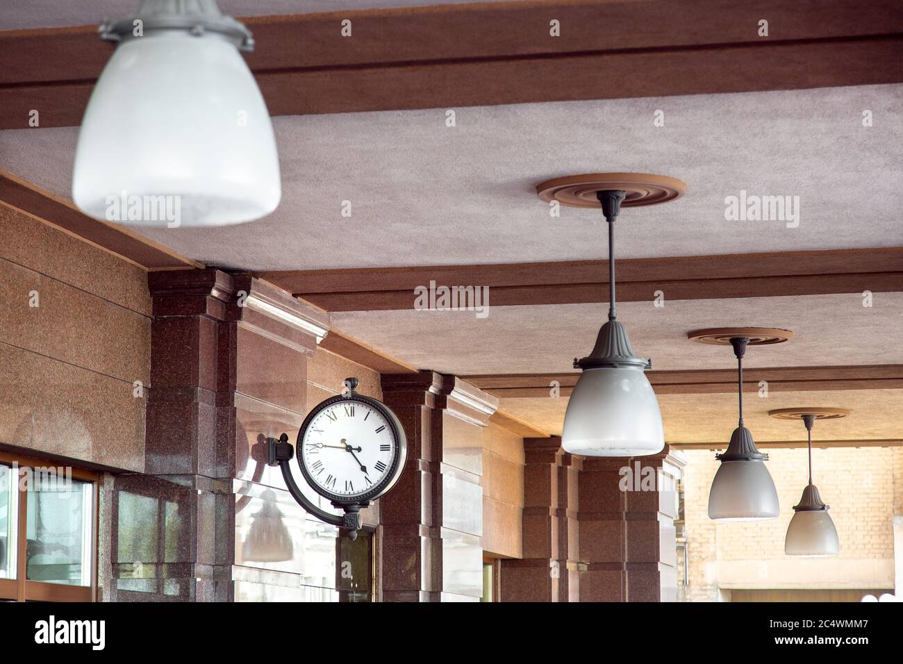 The clock is mounted on a brown marble wall and the ceiling lights are