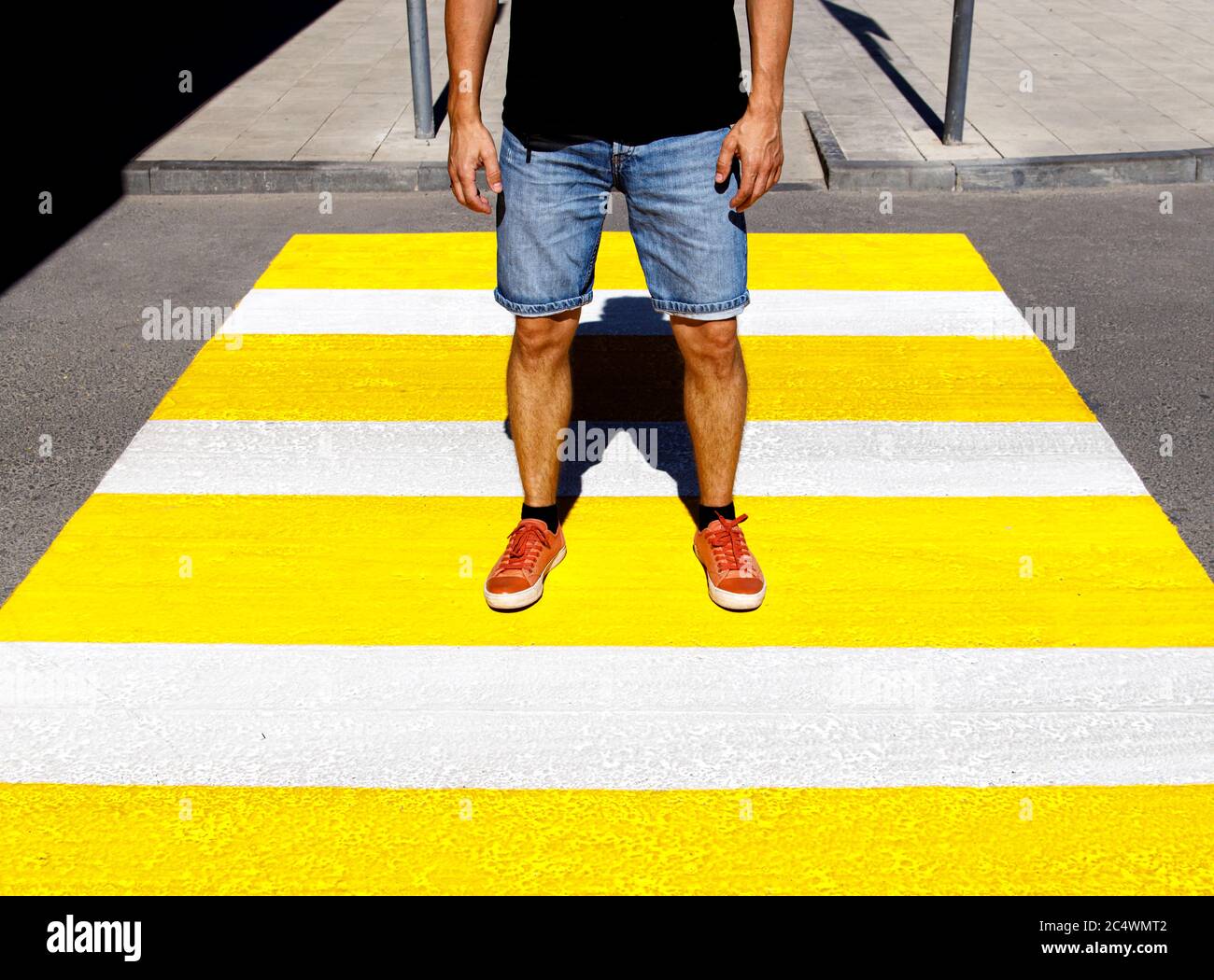 A young man in a black T-shirt and denim shorts stands at a pedestrian crossing Stock Photo