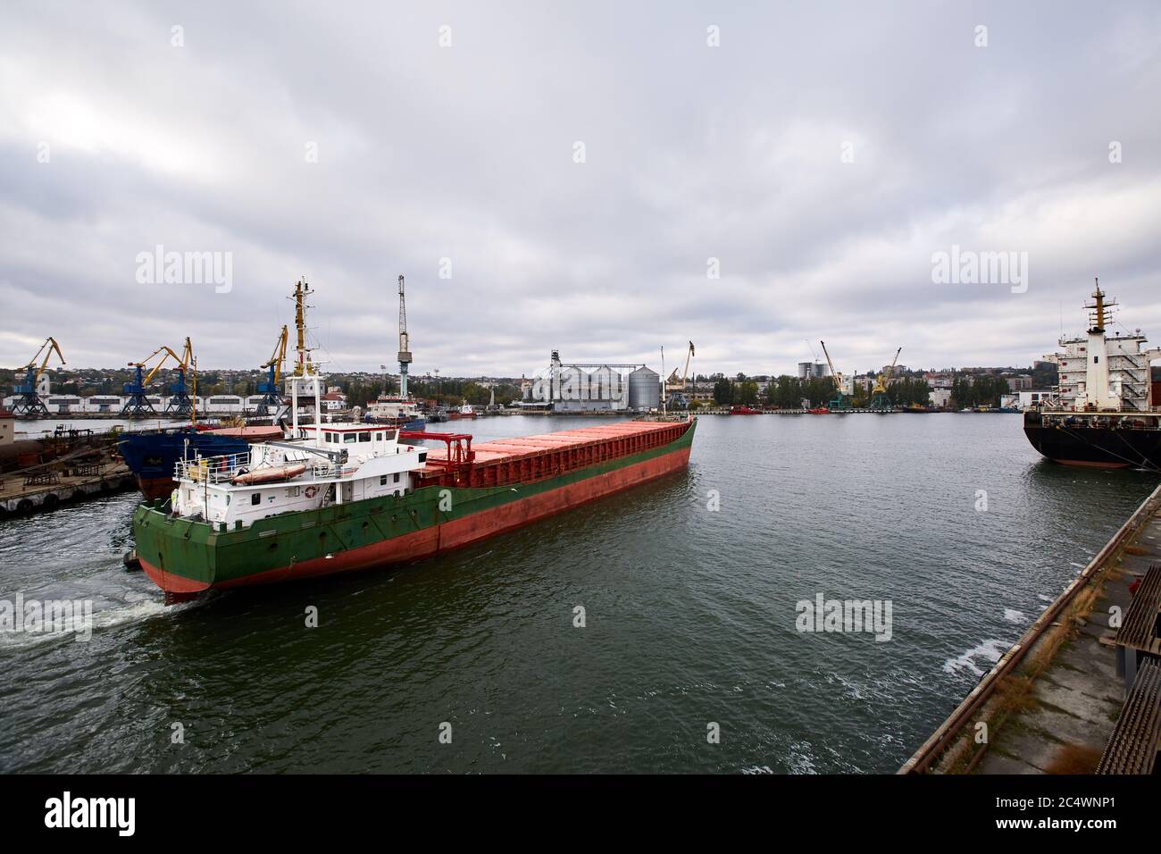Large bulk ship entering the harbour of commercial dock at seaport to load at grain terminal elevators with wheat and other crops. Stock Photo