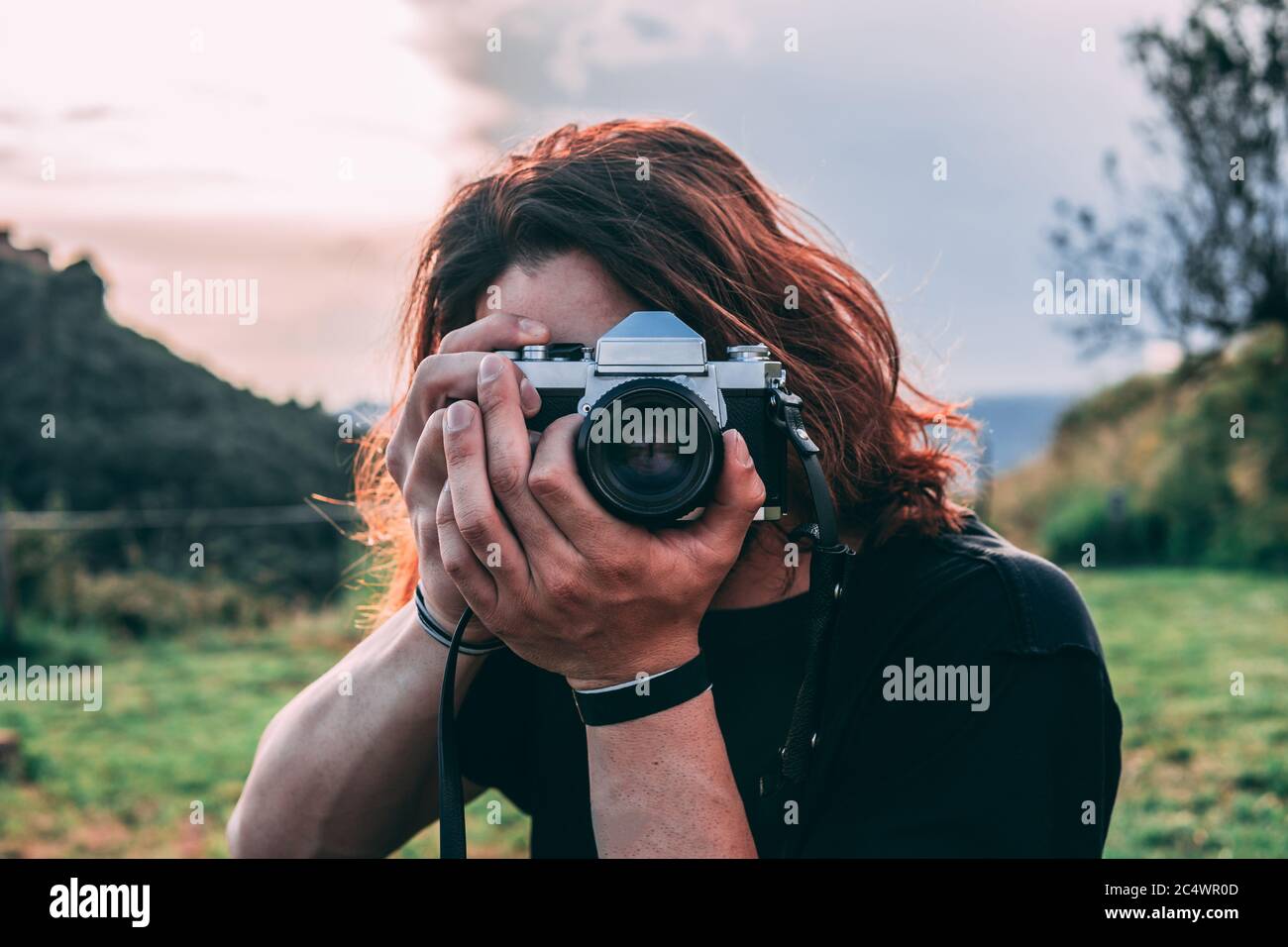 Handsome young man takes a picture facing the camera. He is in the middle of nature and has long and wild hair. Stock Photo