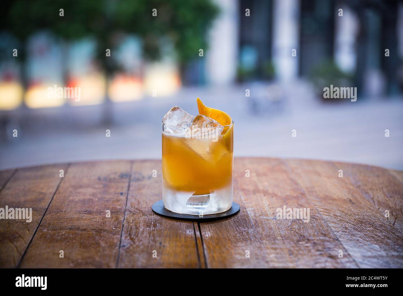 you can see a tasty yellow-colored cocktail on ice standing on a wooden table and the background is blurred Stock Photo