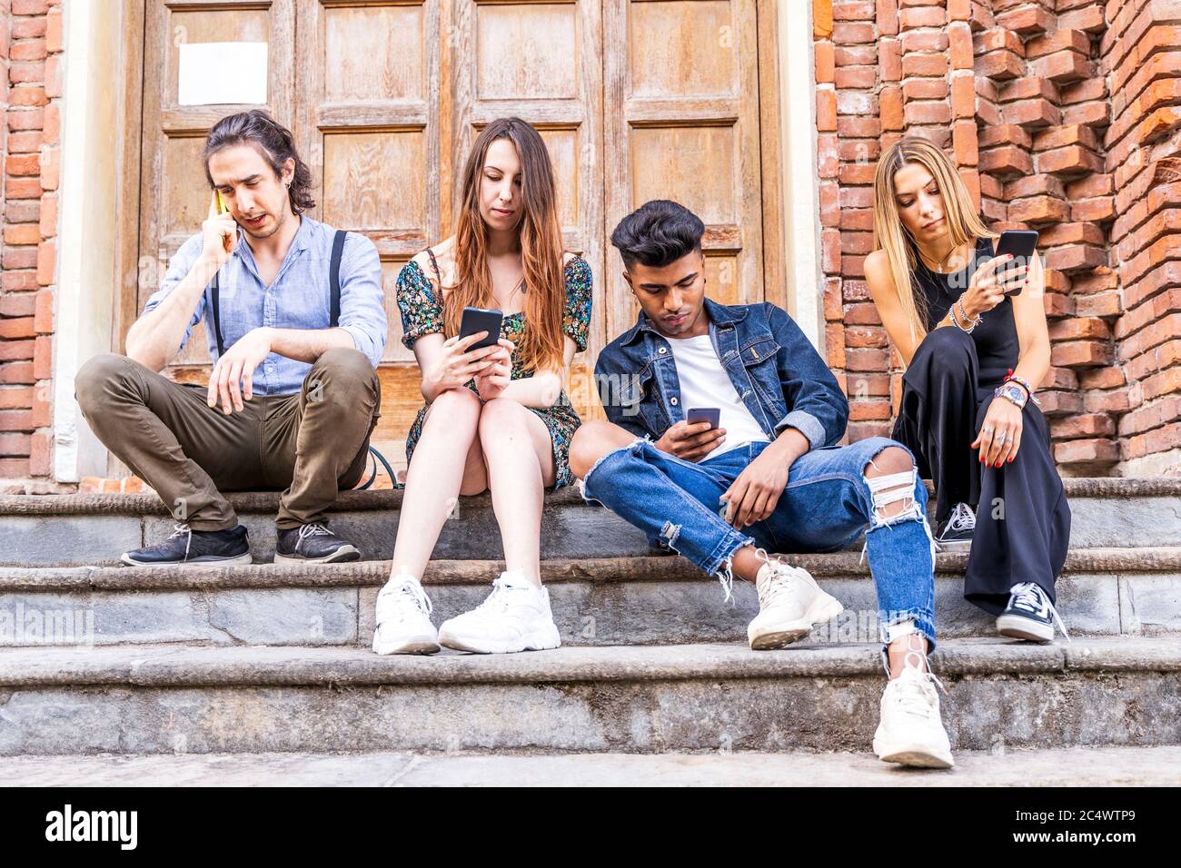 group of multiracial friends sitting on a marble staircase using smartphones to share content on social networks Stock Photo