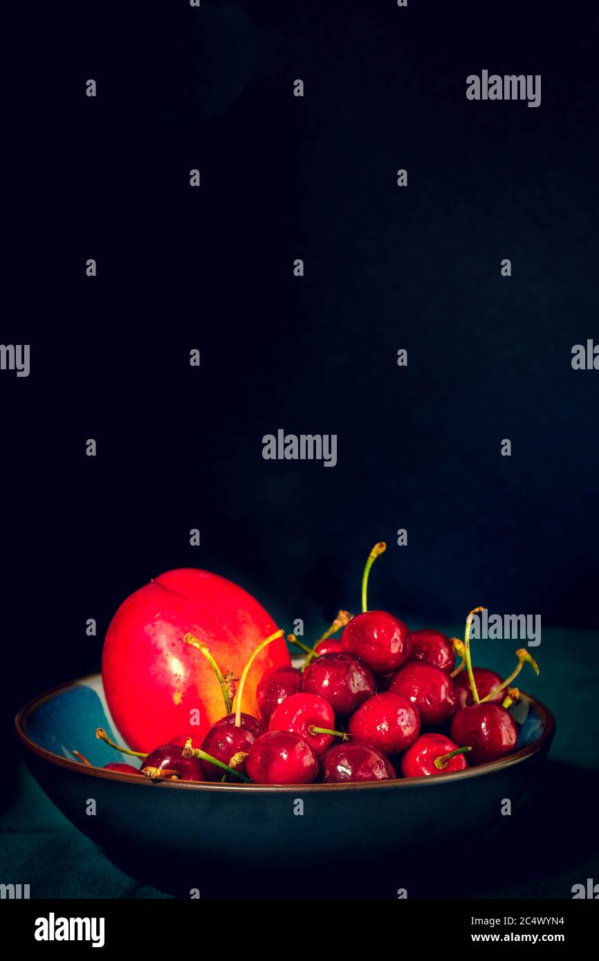 Bowl of cherries and nectarine on dark background, with negative space Stock Photo
