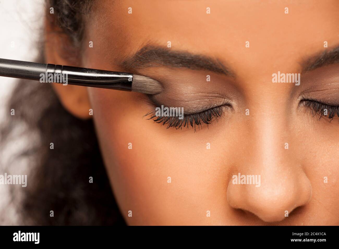 portrait of a young dark-skinned woman applying eye shadow with brush on a white background Stock Photo
