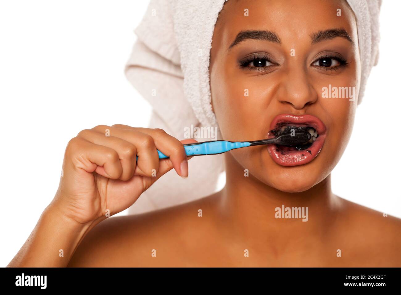 portrait of a happy young dark-skinned woman brushing her teeth with black toothpaste on a white background Stock Photo