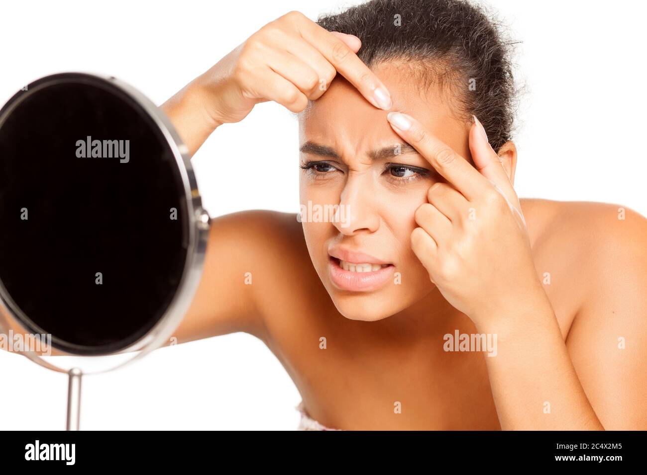 portrait of young dark-skinned woman squeeze a pimple on her forehead on white background Stock Photo