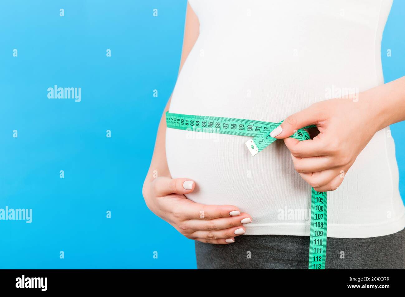 Close up image of tape measure on pregnant woman's belly at blue