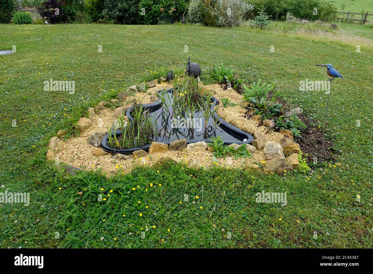 Preformed black plastic garden pond surrounded by gravel path in lawn