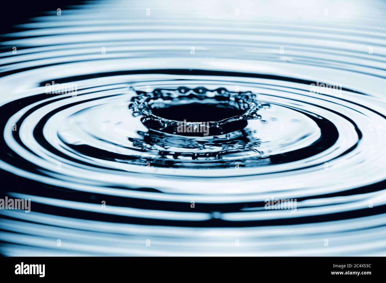 Water splash in dark blue color with a drop of water flying from above. Stock Photo
