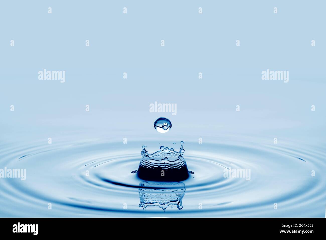 Water splash in dark blue color with a drop of water flying from above Stock Photo