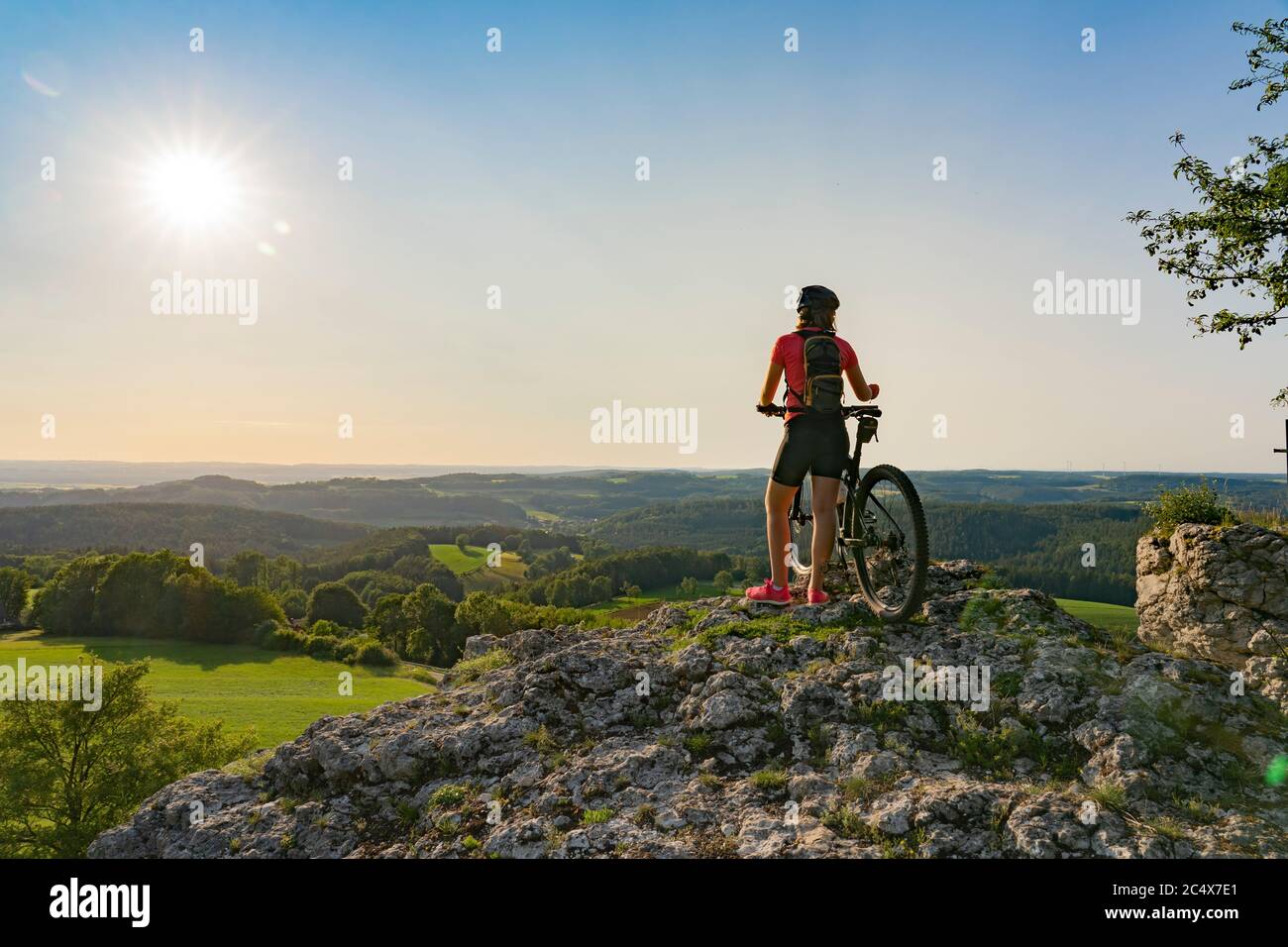 young woman admiring the awesome view over Frankonian Switzerland, during a mountain bike trip during golden hour in the evening Stock Photo