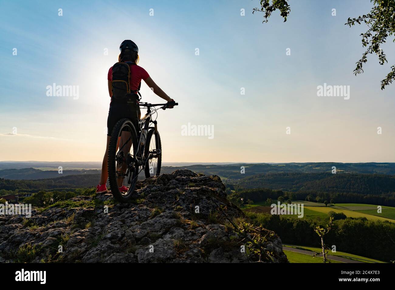 young woman admiring the awesome view over Frankonian Switzerland, during a mountain bike trip during golden hour in the evening Stock Photo