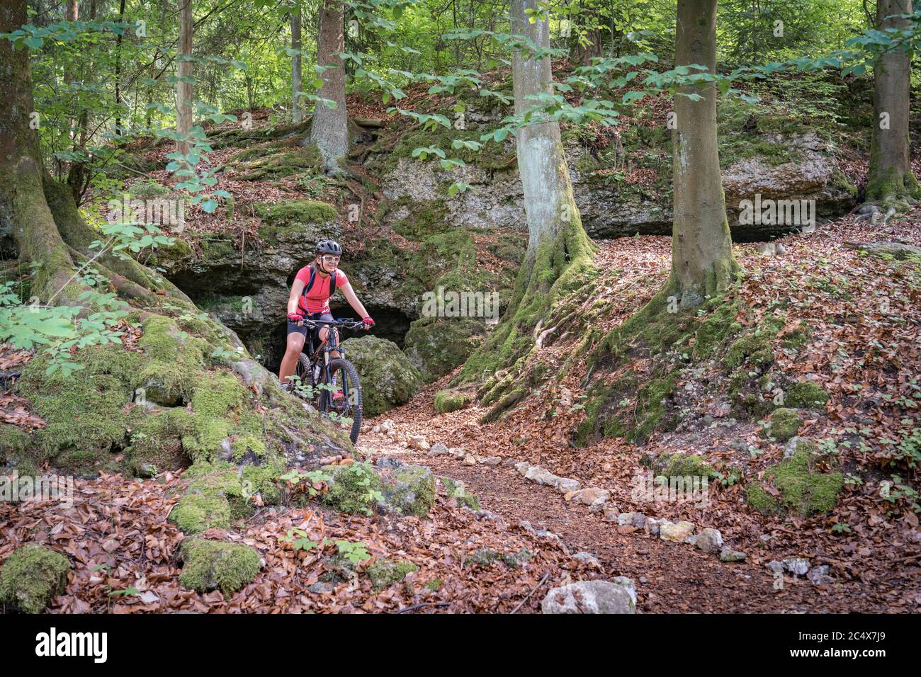 teenage girl riding her mountainbike on a forest trail in front of a cave in Franconian Switzerland, Bavaria, Germany Stock Photo