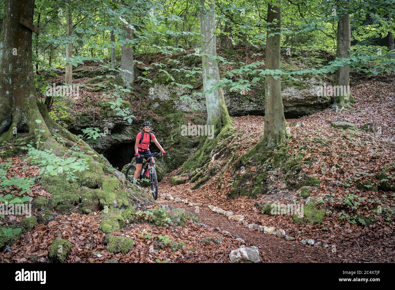 pretty senior woman underway on her electric mountain bike on a rocky forest trail in Franconian Switzerland, Bavaria, Germany Stock Photo