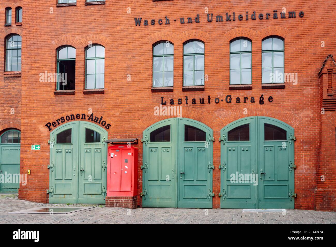 Beautiful industrial red brick facade with three vintage green garage doors. Former truck garage in the courtyard of the Kulturbrauerei Cultural Cente Stock Photo
