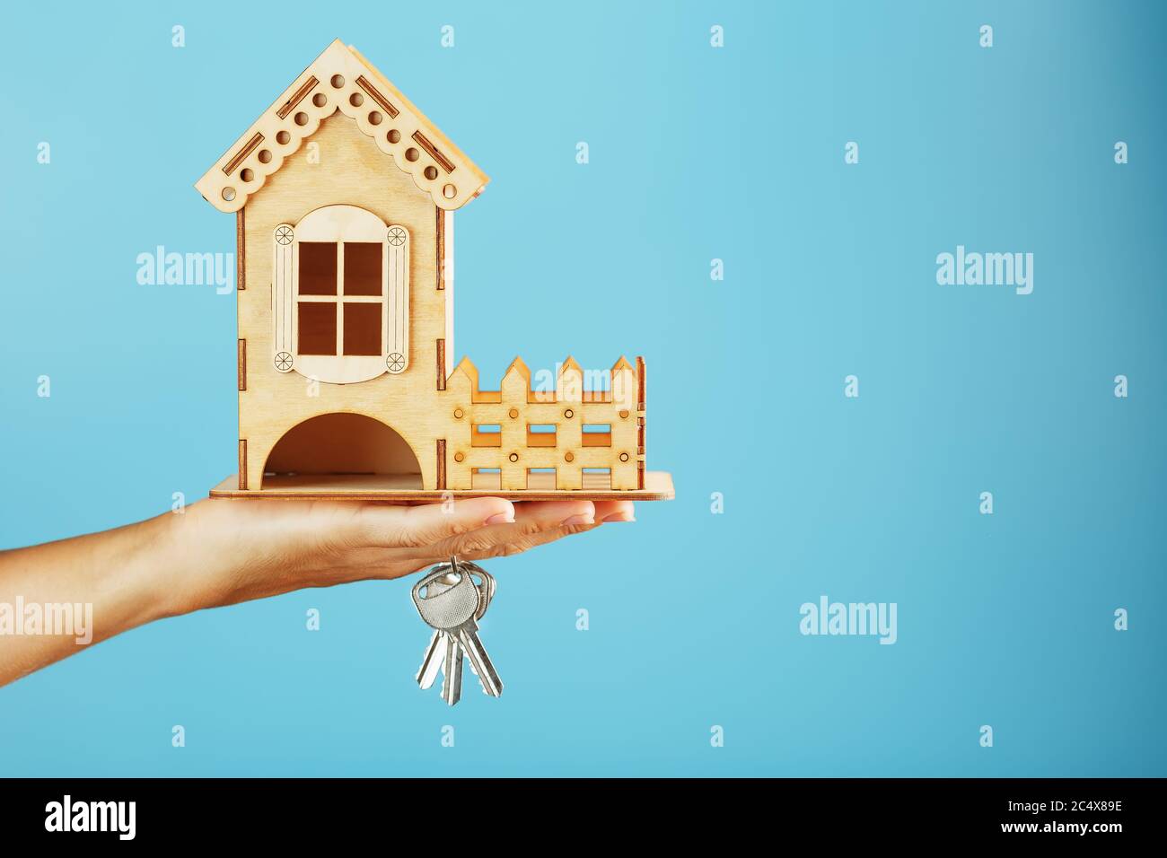 Model of a wooden house in the palm of your hand with keys on a blue ...