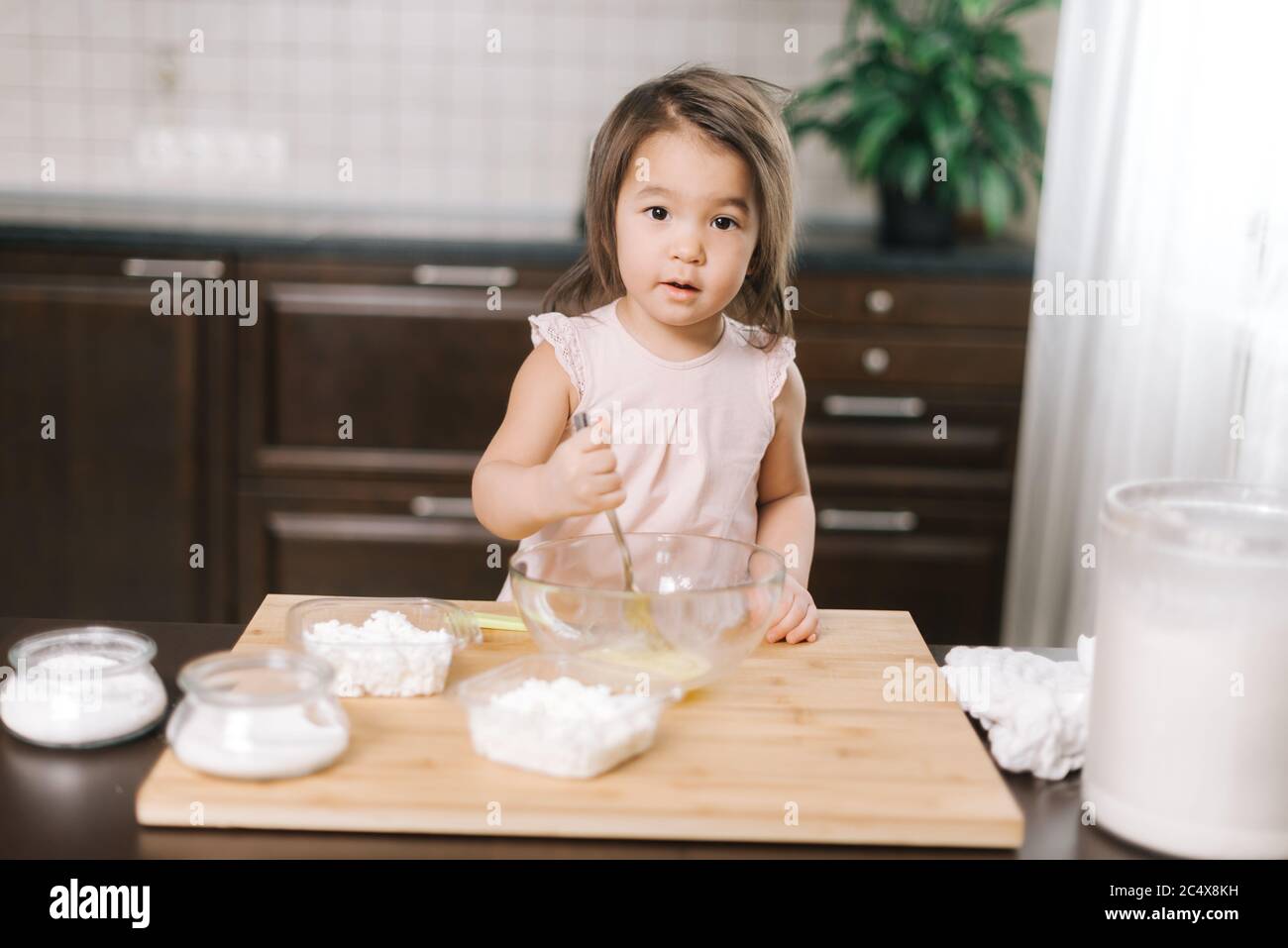 Lovely cute little girl wearing white dress is whisking eggs in mixing