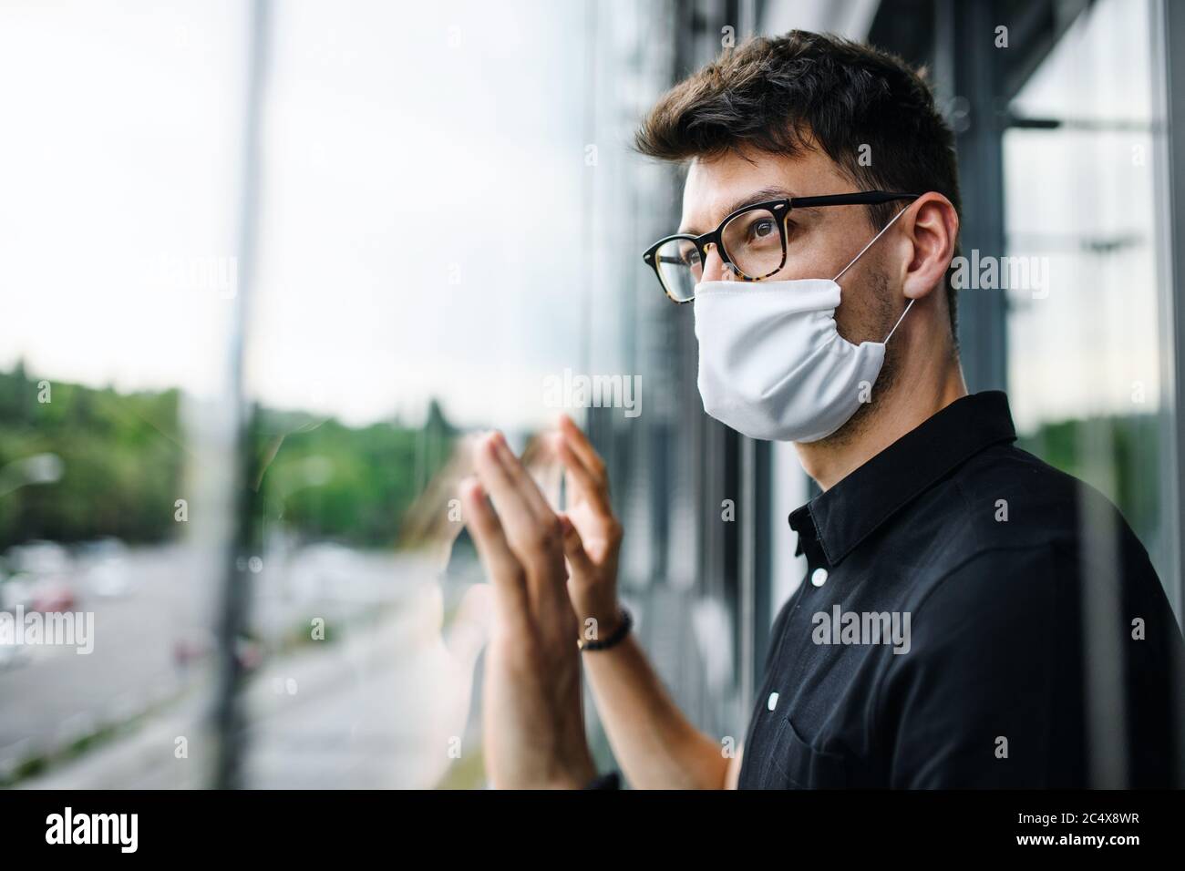 Sad man with face mask looking out through window, quarantine and lockdown concept. Stock Photo