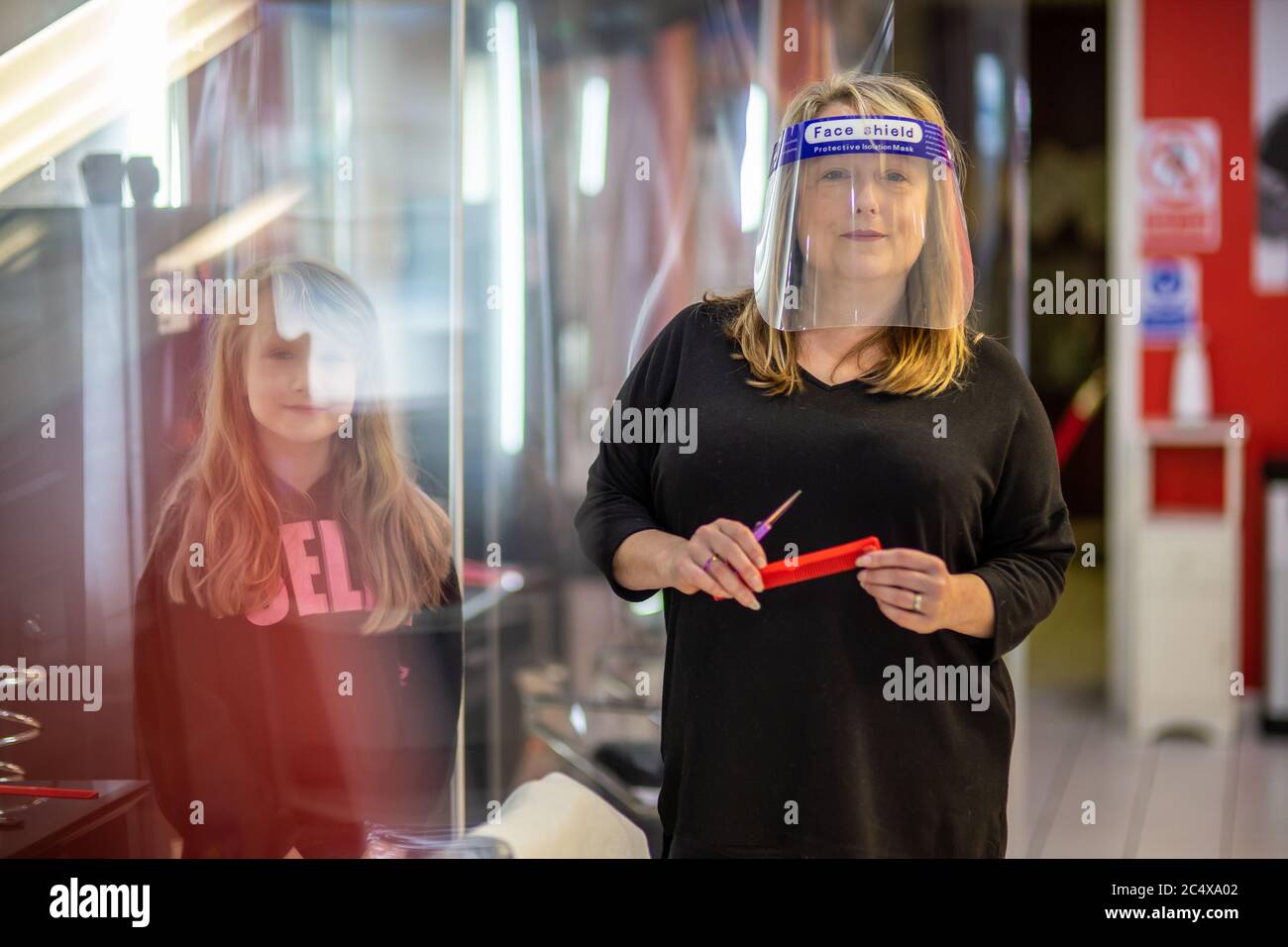 Hairdresser wearing face shield in a salon, after opening due to