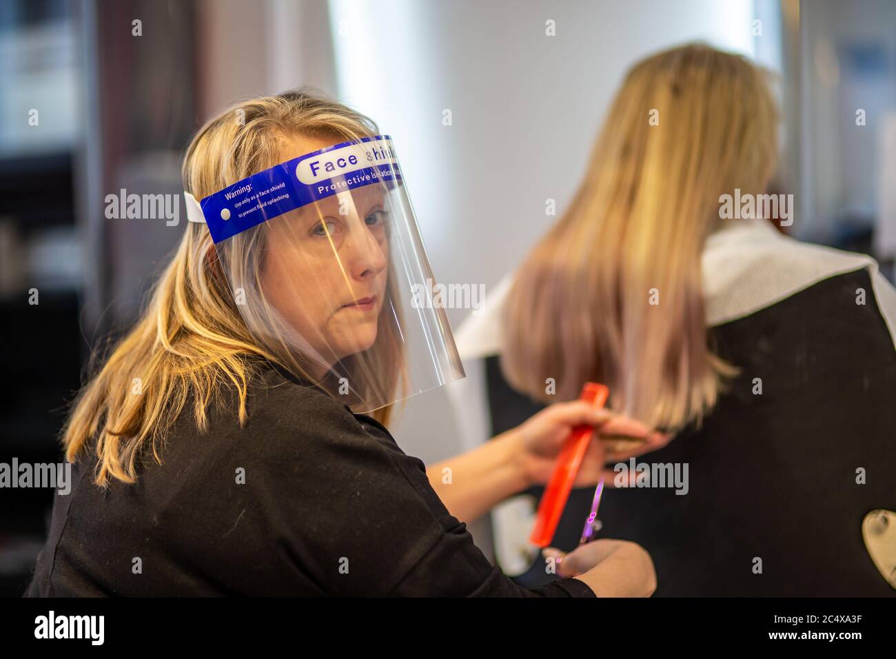 Hairdresser wearing face shield in a salon, after opening due to