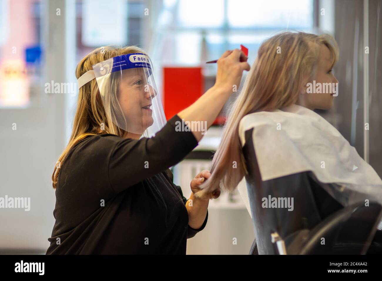 Hairdresser wearing face shield in a salon, after opening due to