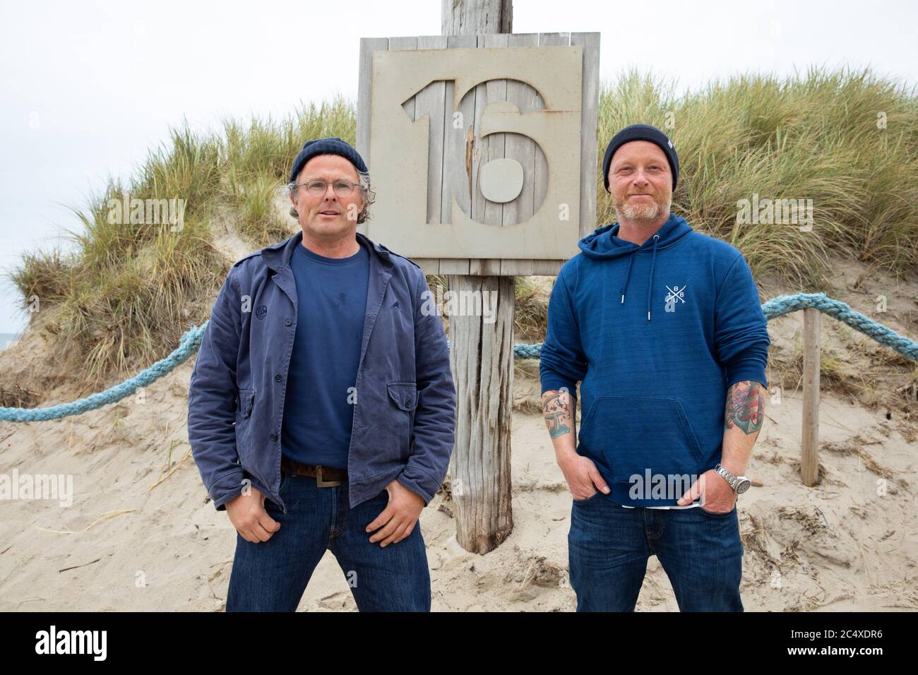 11 June 2020, Schleswig-Holstein, Kampen (Sylt): The cousins Sven Behrens  and Tim Behrens (r), manager of the bistro "Buhne 16", are standing in  front of a wooden sign at the entrance to