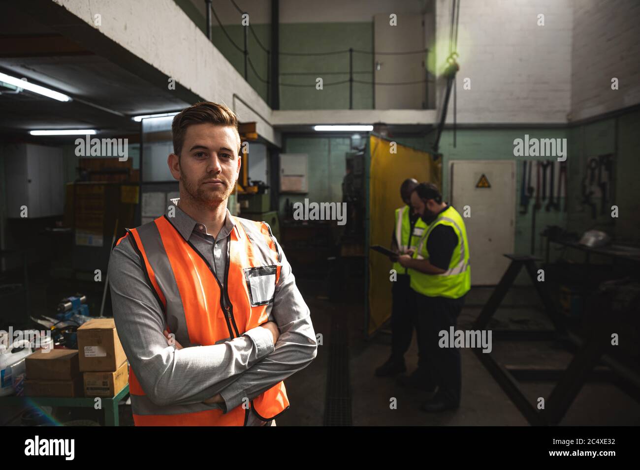 Male factory worker wearing a Hi-vis vest standing with his arms crossed at the factory Stock Photo