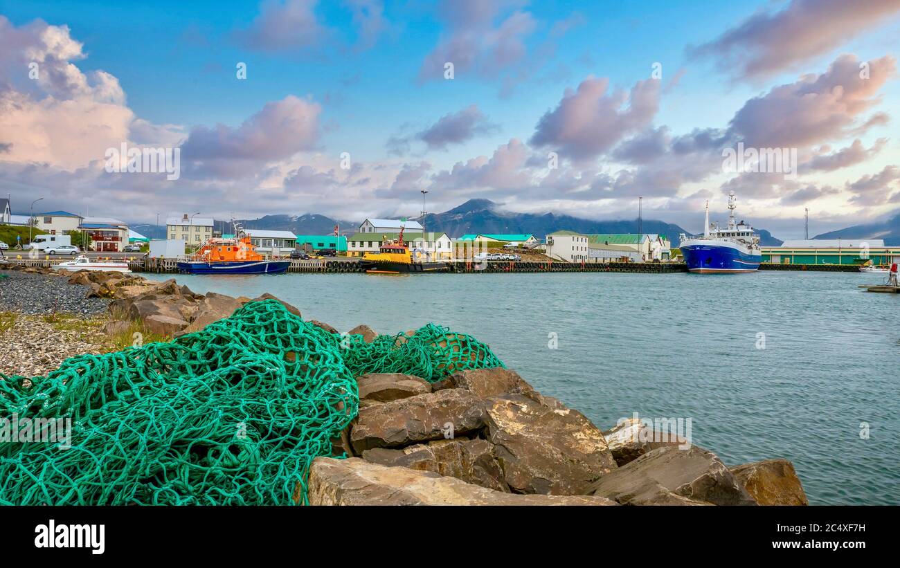 A green fishing net in the foreground of a picturesque landscape shot of a small, colorful fishing village on the coast of West Iceland. Stock Photo