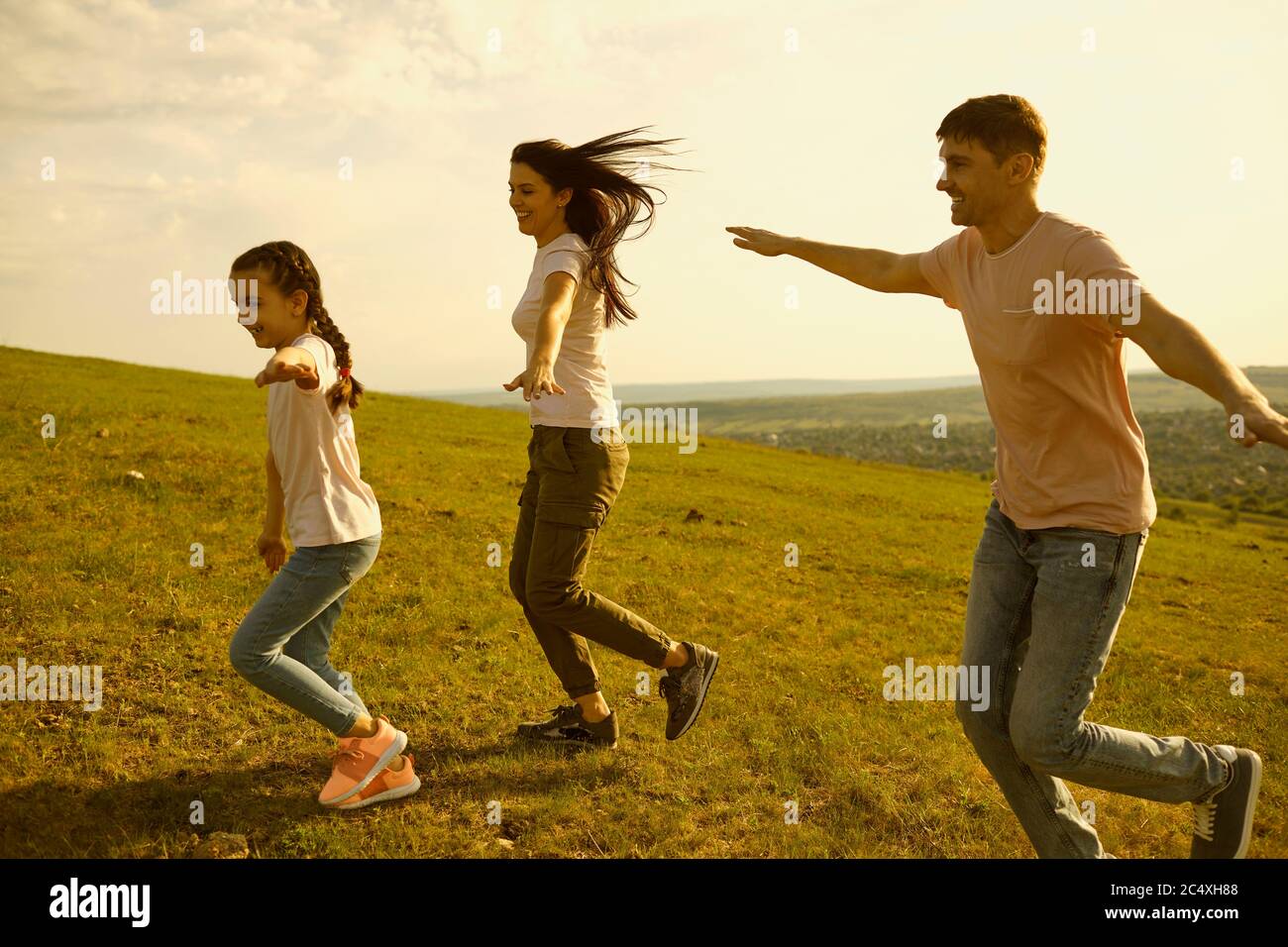 Joyful family with mom, dad and little kid running in mountains. Parents with child having fun playing airplane game Stock Photo